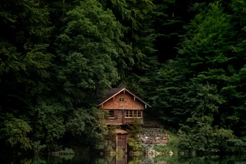 A wooden cabin beside a lake and forest.