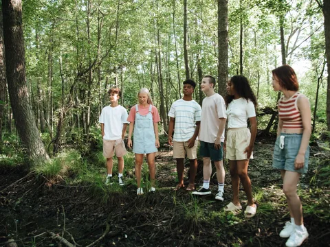 A diverse group of teenagers standing together in a lush summer forest setting.