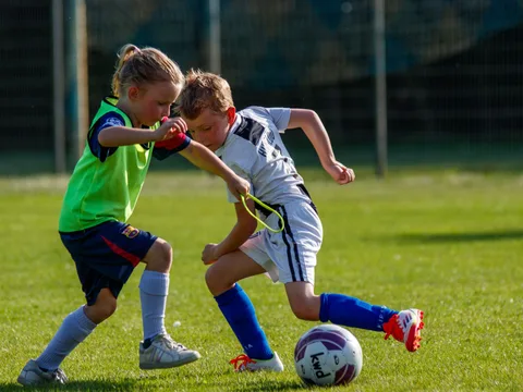 Two kids playing soccer on a sunny day.