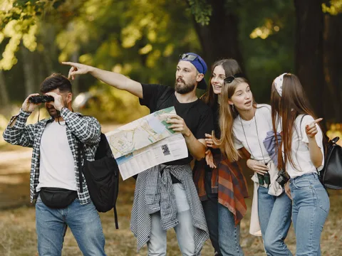 Group of friends navigating nature with map and binoculars, enjoying a summer hike.