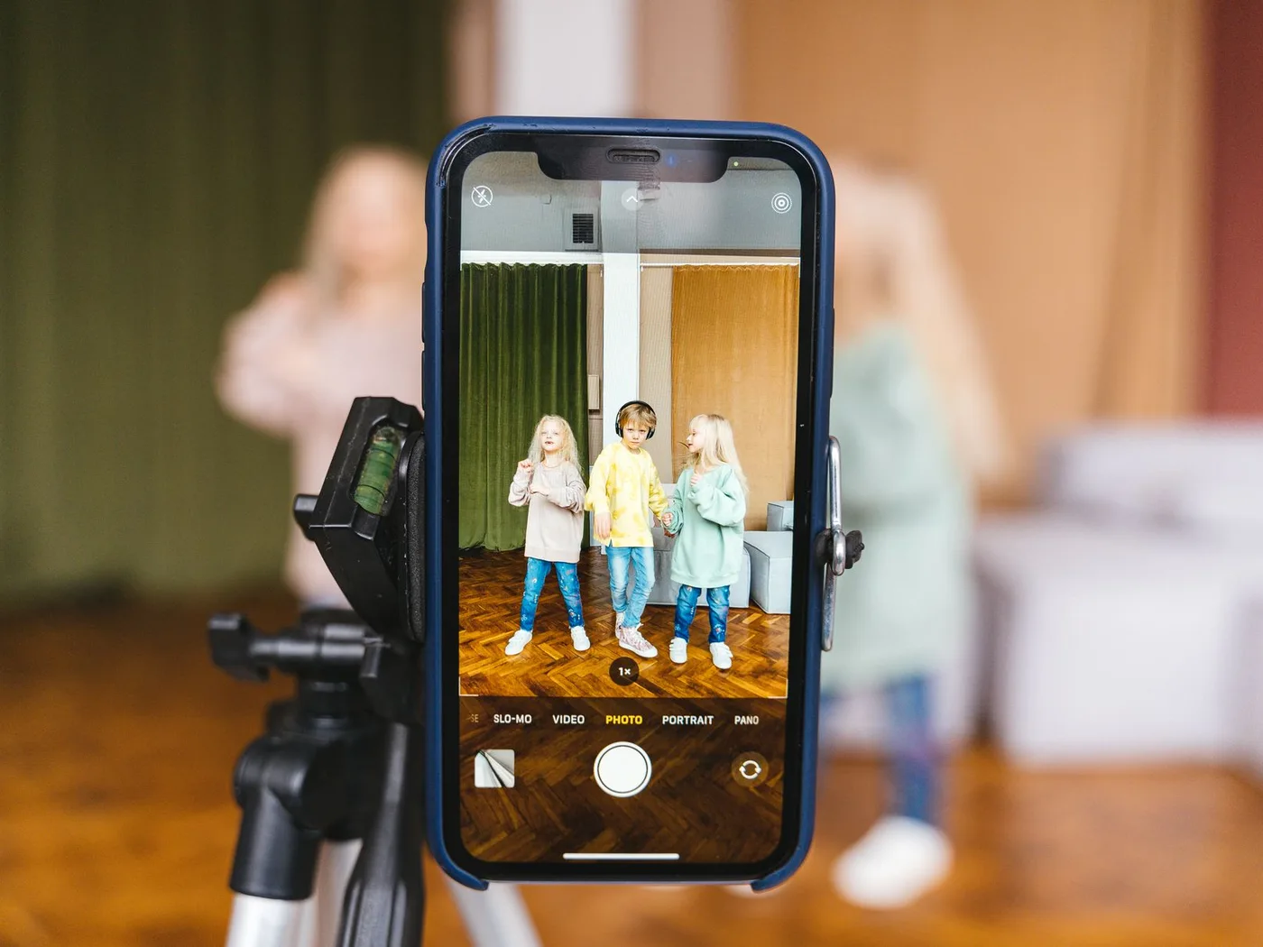 Three children record a video indoors using a smartphone on a tripod.