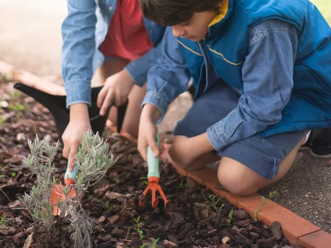 Two children gardening outdoors in Portugal, engaging with soil and plants.