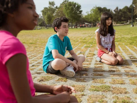 Kids sitting together in a green park during summer camp for team building and fun.