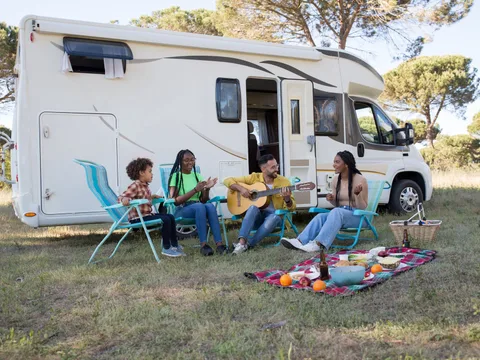 A family relaxing outdoors with a picnic and guitar by their camper, enjoying a sunny summer day in Portugal.