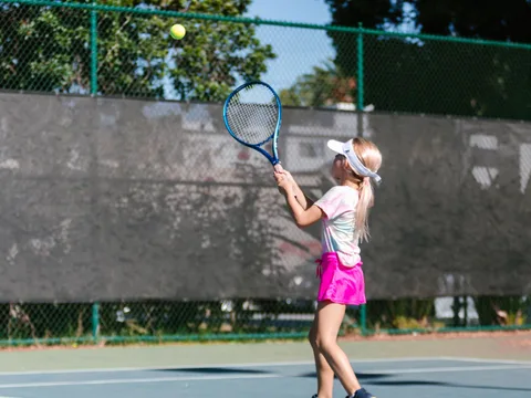 Child engages in tennis practice on an outdoor court, enjoying a sunny day.