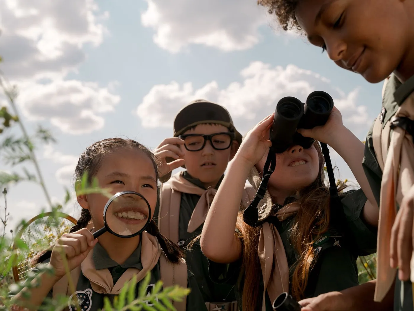 A group of young scouts enjoy outdoor exploration with binoculars and magnifying glass.