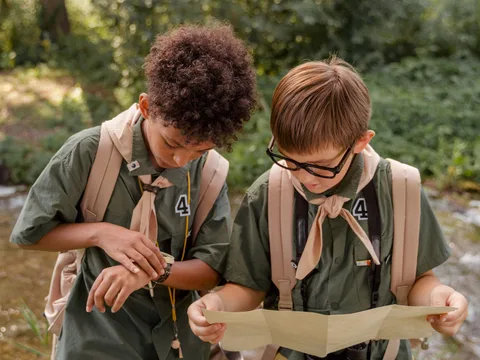 Two boy scouts examining a map in a lush forest.