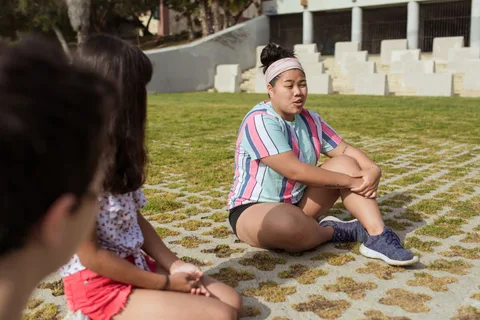 Children sitting together on the grass during an outdoor camp activity.