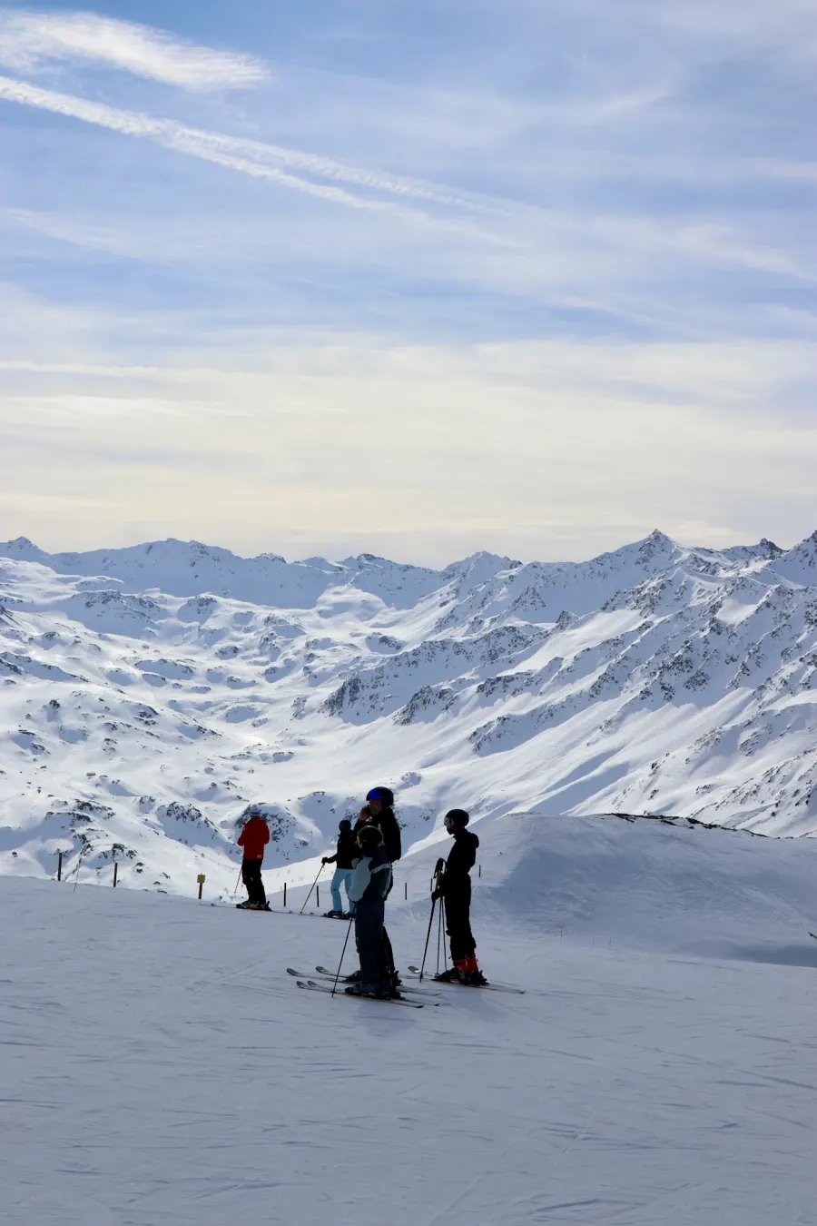 Skiers on a snowy mountain slope below alpine peaks